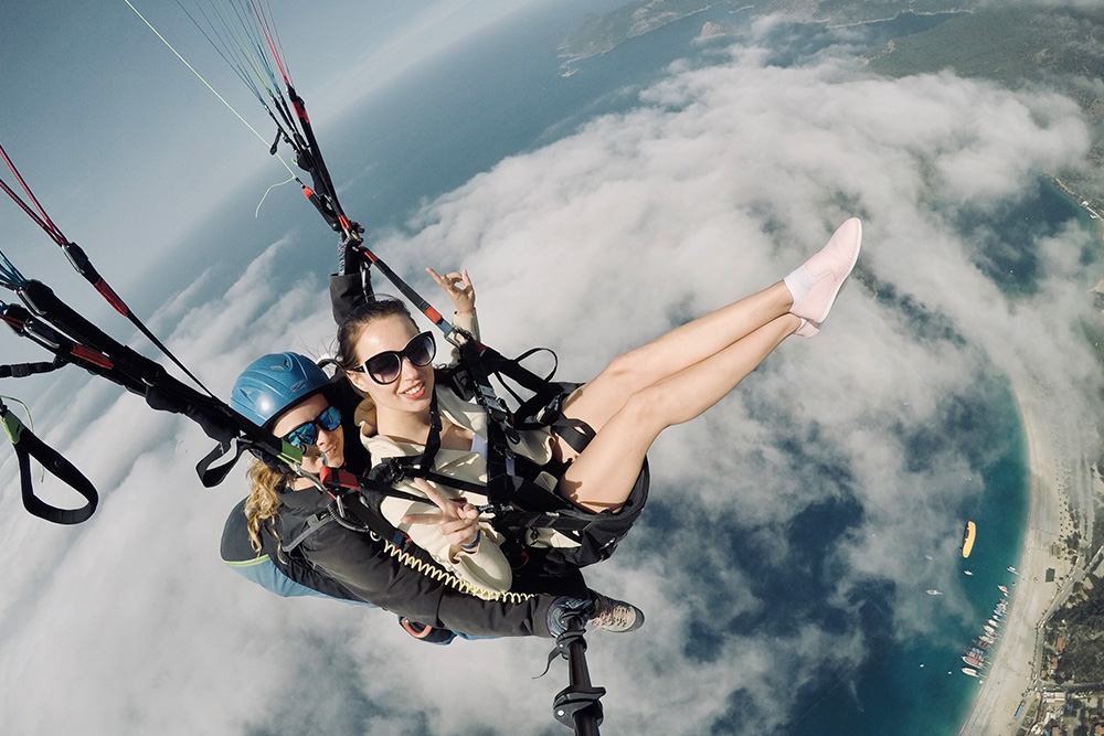 Woman with instructor flying on parachute against sky Vuelos Biplaza - Imagen 1
